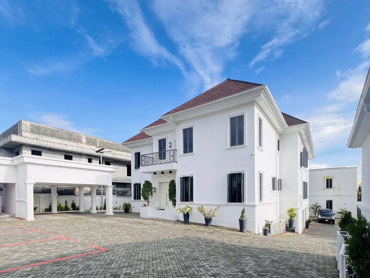 After — Two-storey residence by HAMAAR Projects shown at bare concrete and blockwork stage against a blue sky, and as the completed modern white facade