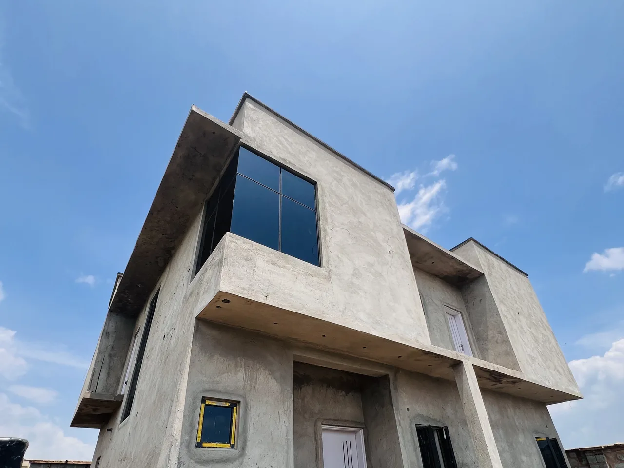 Before — Two-storey residence by HAMAAR Projects shown at bare concrete and blockwork stage against a blue sky, and as the completed modern white facade